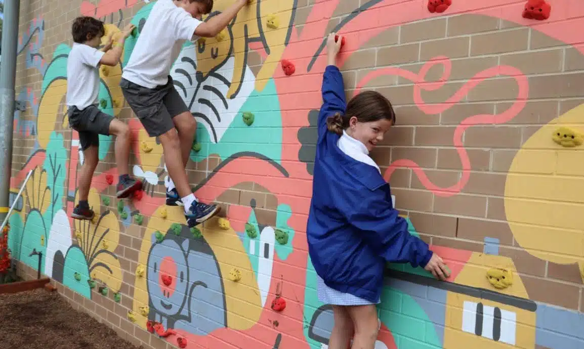 Children enjoying a colorful outdoor climbing wall at a playground, designed by an innovator.